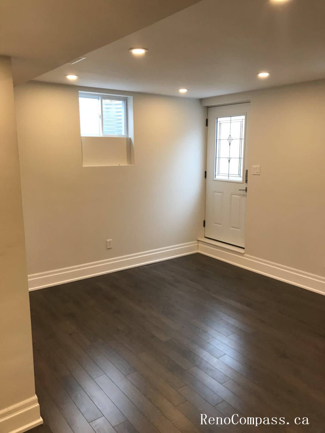 This image showcases a bright finished basement entry area in a Richmond Hill home, featuring dark hardwood flooring, recessed LED lighting, smooth ceilings, and a clean white exterior door. The renovated space provides a functional and modern secondary entrance. Renovation completed by Reno Compass Inc.