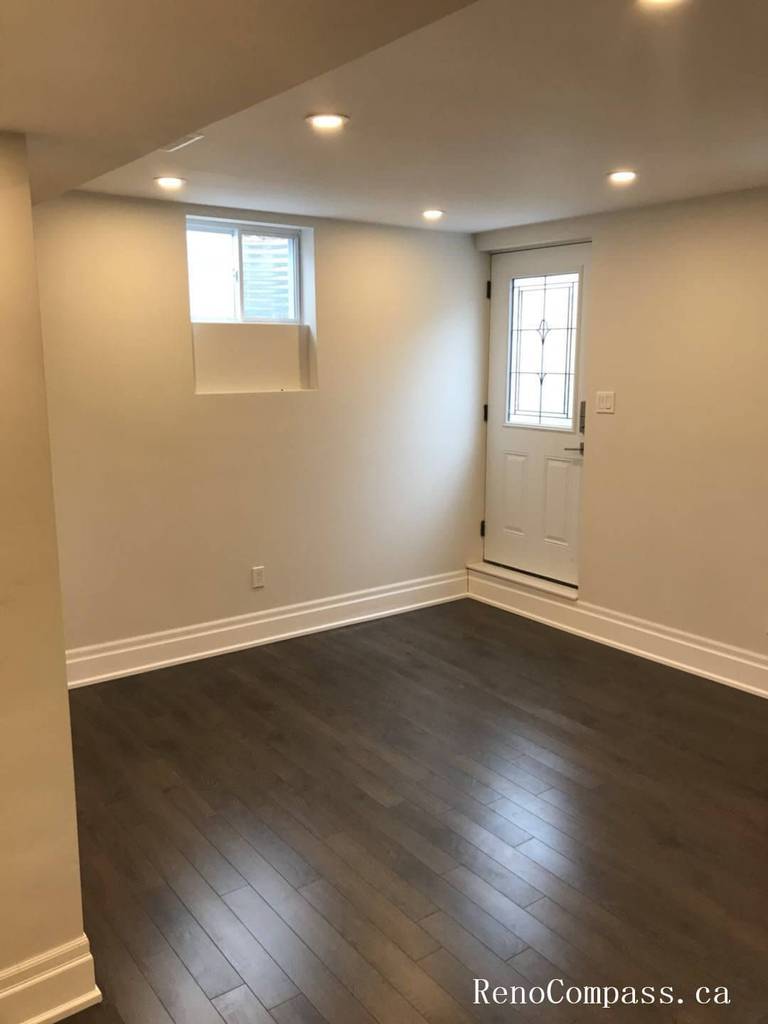 This image showcases a bright finished basement entry area in a Richmond Hill home, featuring dark hardwood flooring, recessed LED lighting, smooth ceilings, and a clean white exterior door. The renovated space provides a functional and modern secondary entrance. Renovation completed by Reno Compass Inc.