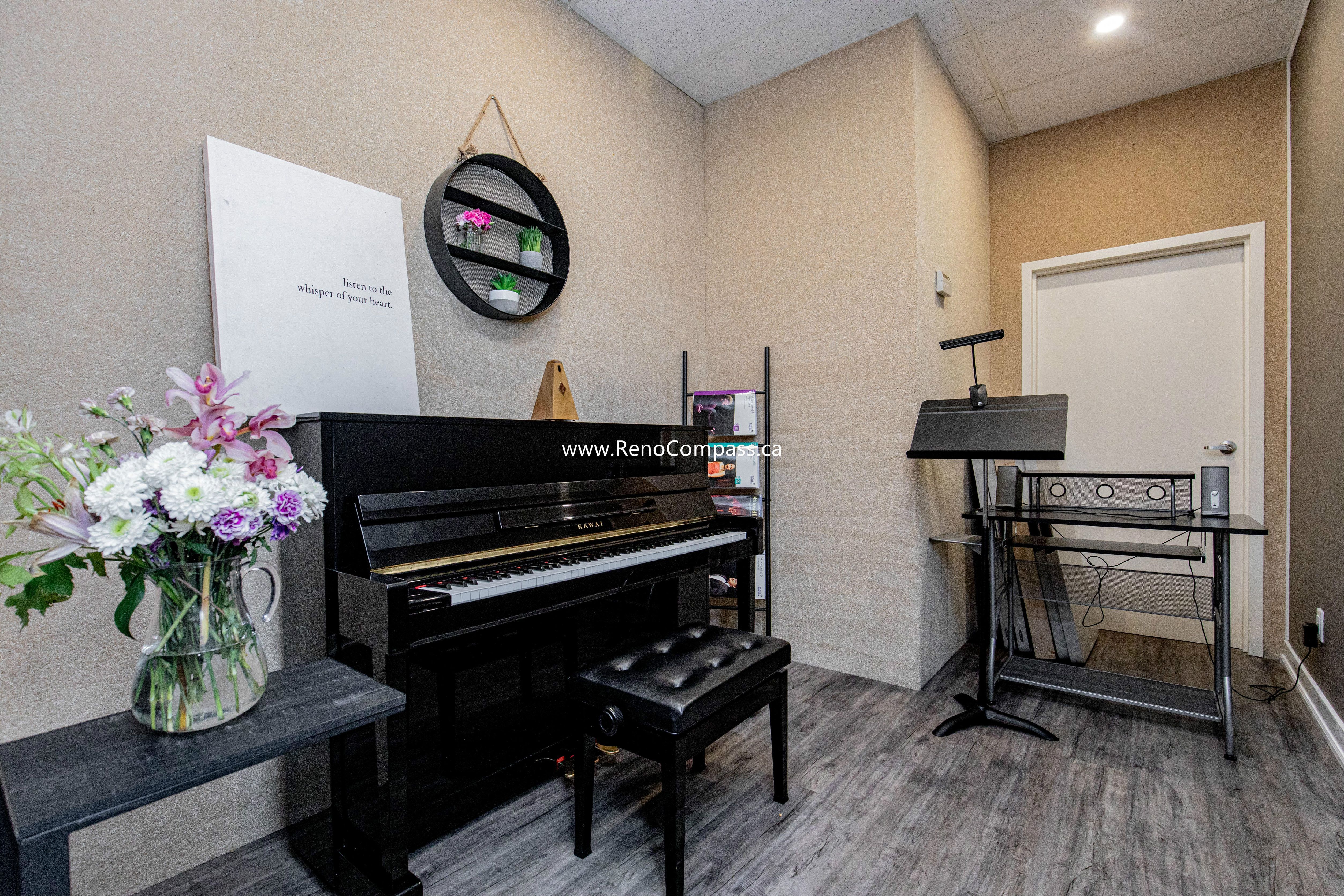 A cozy and professional private lesson room at The Singing School. This commercial interior features modern grey wood laminate flooring, custom textured wall finishes, and a glimpse into a feature room with industrial brick-style wallpaper. Expert commercial contracting in Richmond Hill.