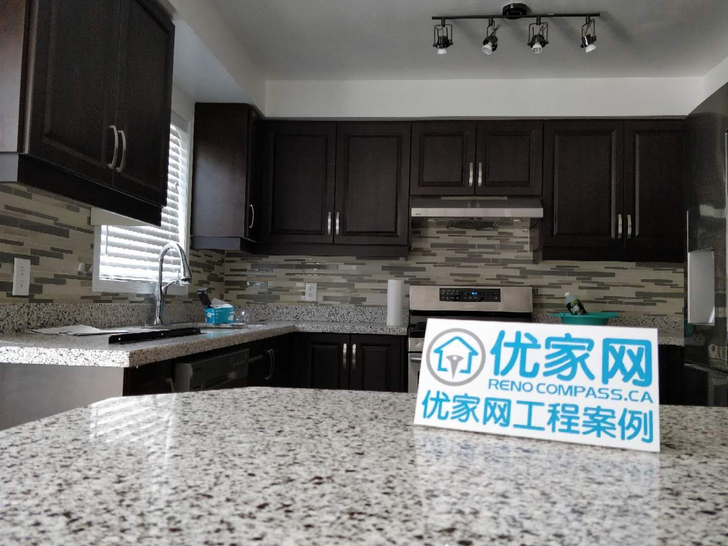 This kitchen renovation project in Ajax showcases a modern upgrade featuring dark wood cabinetry, granite countertops, and a contemporary mosaic backsplash. The layout enhances both functionality and aesthetics, with improved lighting and efficient use of space. As part of a full interior and exterior house renovation, this kitchen reflects high-quality craftsmanship and practical design solutions for everyday living.