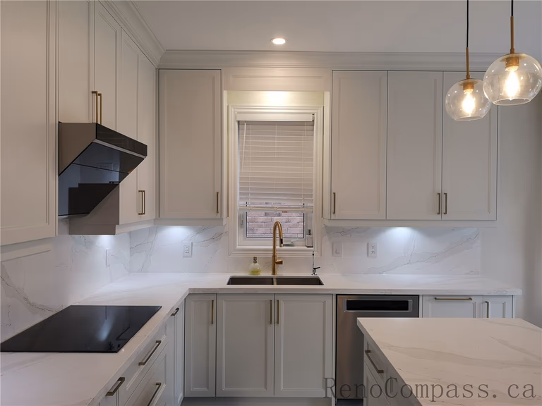 This Aurora kitchen renovation showcases a modern and elegant layout with custom white shaker cabinets, quartz countertops, marble-style backsplash, and stylish brushed gold hardware. Under-cabinet lighting enhances both functionality and ambiance, while the centered window sink design creates a bright and balanced workspace. Completed by a professional Toronto renovation company focused on quality craftsmanship, timeless design, and practical everyday living.