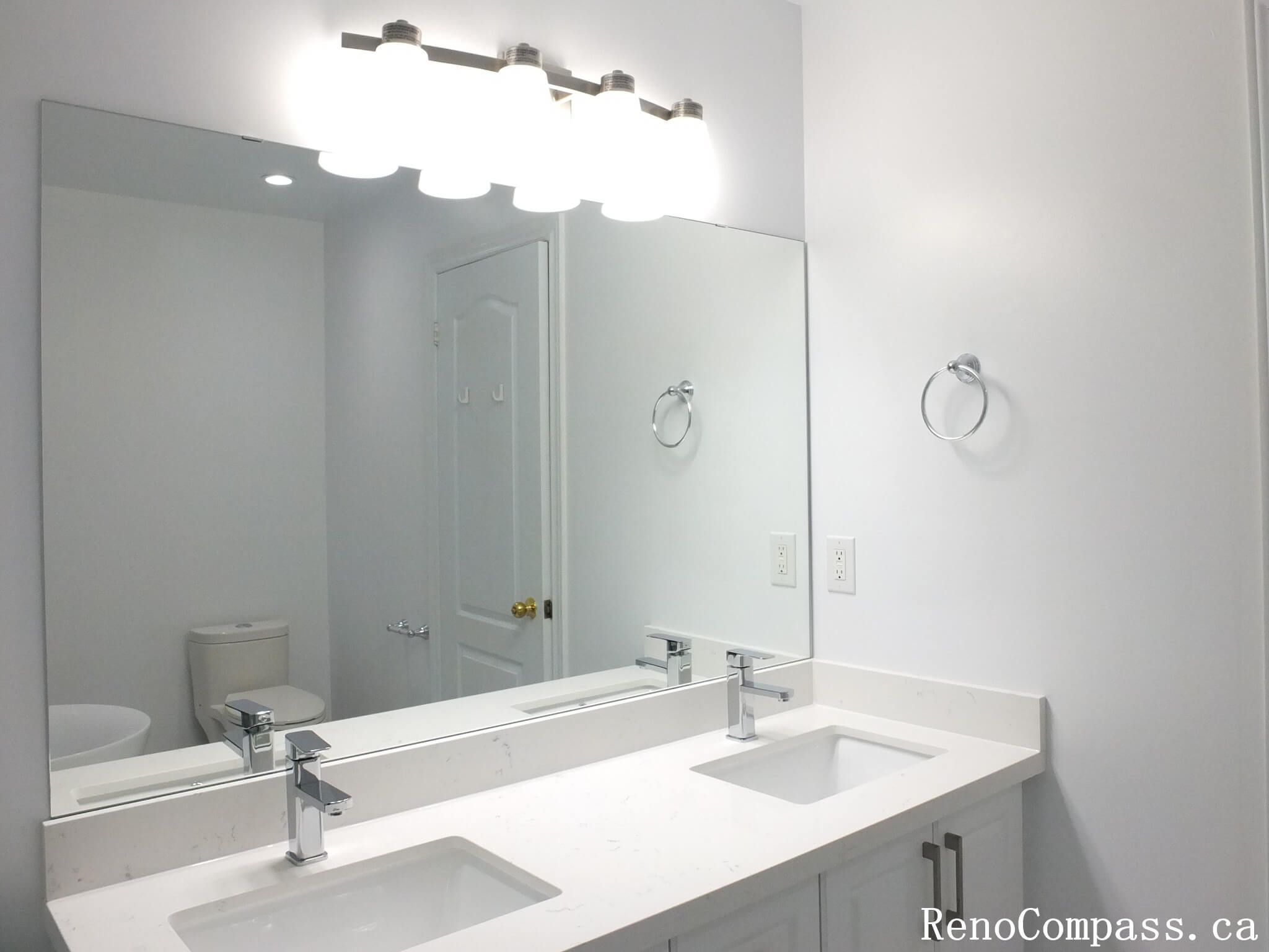 This Richmond Hill bathroom renovation features a modern double-sink vanity with a sleek quartz countertop and full-width mirror enhanced by bright LED vanity lighting. Completed by a professional Toronto renovation company, the space is designed for improved functionality, balanced illumination, and clean contemporary aesthetics. The streamlined fixtures and neutral palette create a bright, organized, and practical bathroom layout ideal for everyday family use.