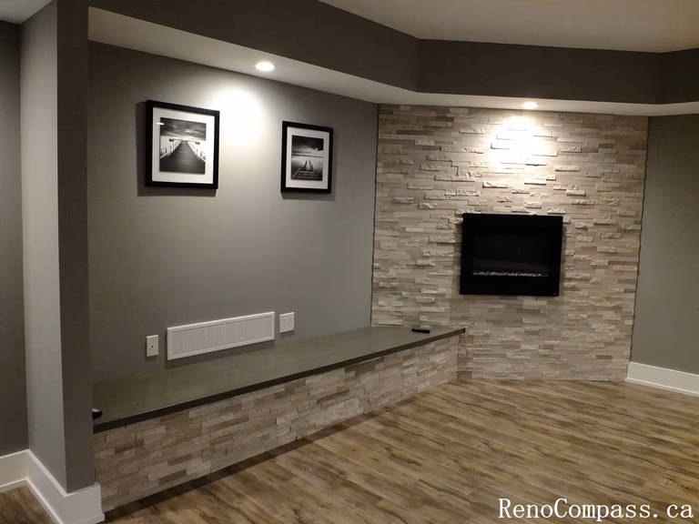 Modern finished basement in Waterloo featuring a stunning stone feature wall, built‑in electric fireplace, recessed lighting, and a custom bench with matching stone accents. A stylish focal point in the renovated lower level.