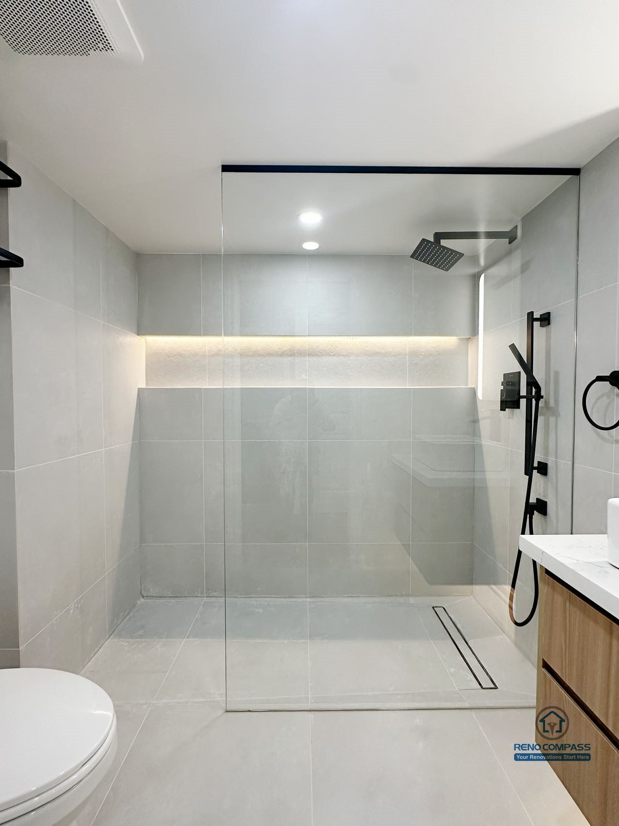 This bathroom renovation features a clean curbless shower layout with integrated wall niche lighting and a linear floor drain, creating a seamless and uncluttered visual experience. Large-format tiles, restrained color tones, and matte black fixtures bring balance between modern design and everyday functionality. The shower area is carefully planned to maintain proper drainage while keeping the floor visually continuous, enhancing both comfort and long-term usability.
Location: Thornhill · Toronto Contractor: Reno Compass