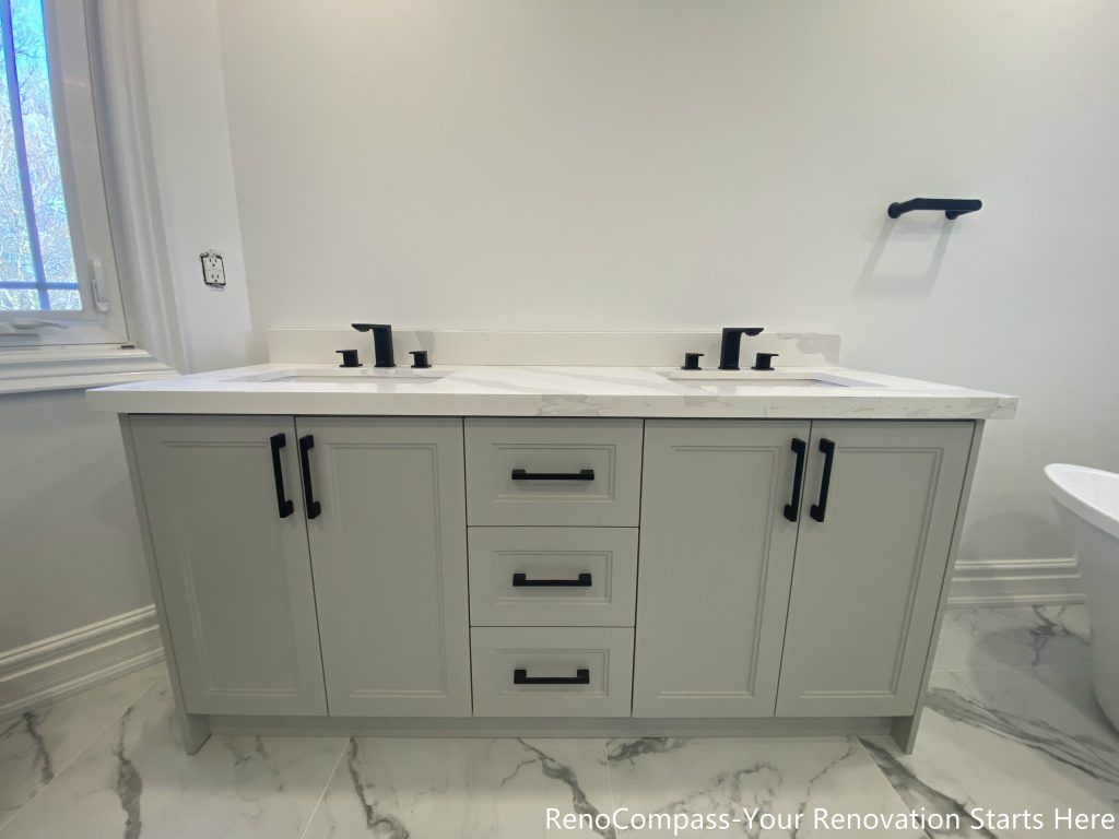 This Thornhill bathroom renovation features a custom double sink vanity finished in a soft gray tone, paired with a marble-look countertop and matte black faucets and cabinet hardware. The symmetrical layout enhances daily functionality for shared use, while integrated storage drawers provide practical organization. Clean lines, neutral colors, and durable materials create a timeless bathroom vanity design that balances aesthetics, comfort, and long-term usability.