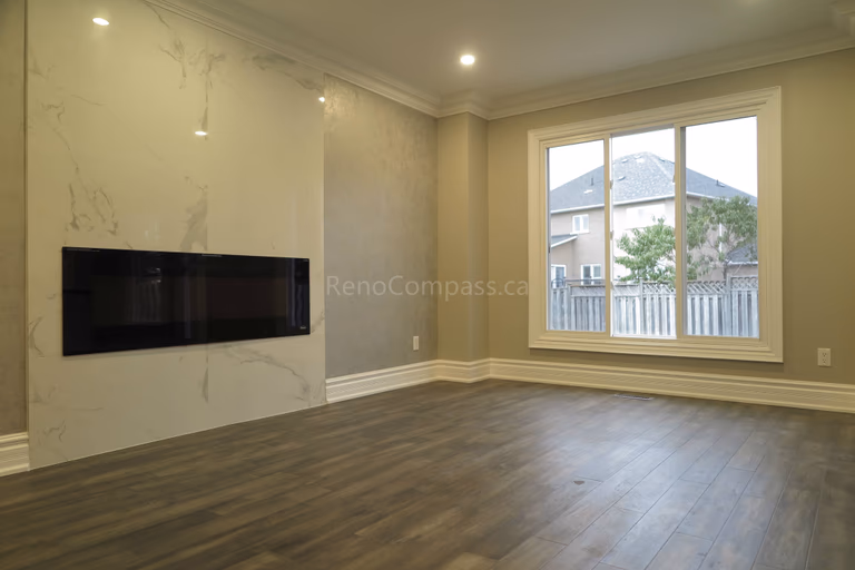 This Markham interior renovation highlights a modern living room upgrade featuring a sleek built-in linear fireplace and a marble-style feature wall. The space is finished with warm neutral paint tones, crown molding details, and newly installed dark hardwood flooring, creating a clean and elegant contemporary atmosphere. Completed by Reno Compass, a trusted renovation contractor providing professional interior renovation and custom finishing services in Markham and the Greater Toronto Area.