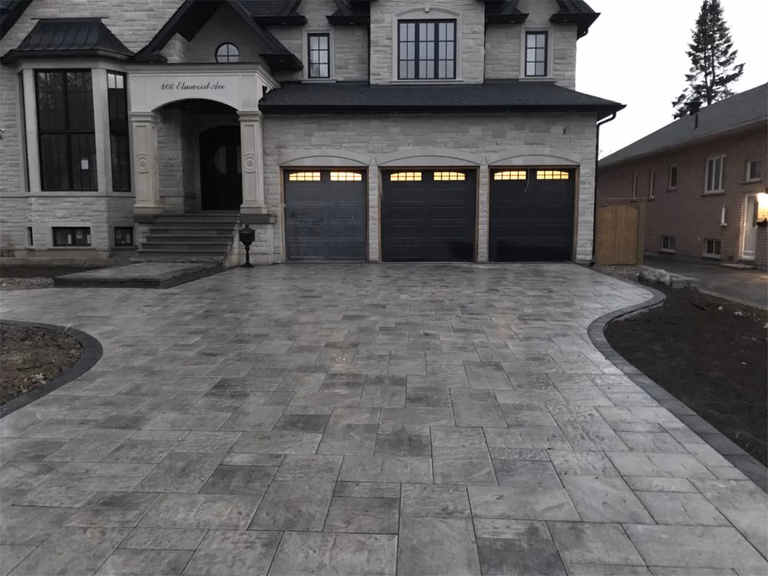 Luxury home front yard landscaping project in Toronto featuring large-format interlocking driveway stones, curved driveway layout, and elegant entrance design that enhances curb appeal and complements the modern residential architecture.