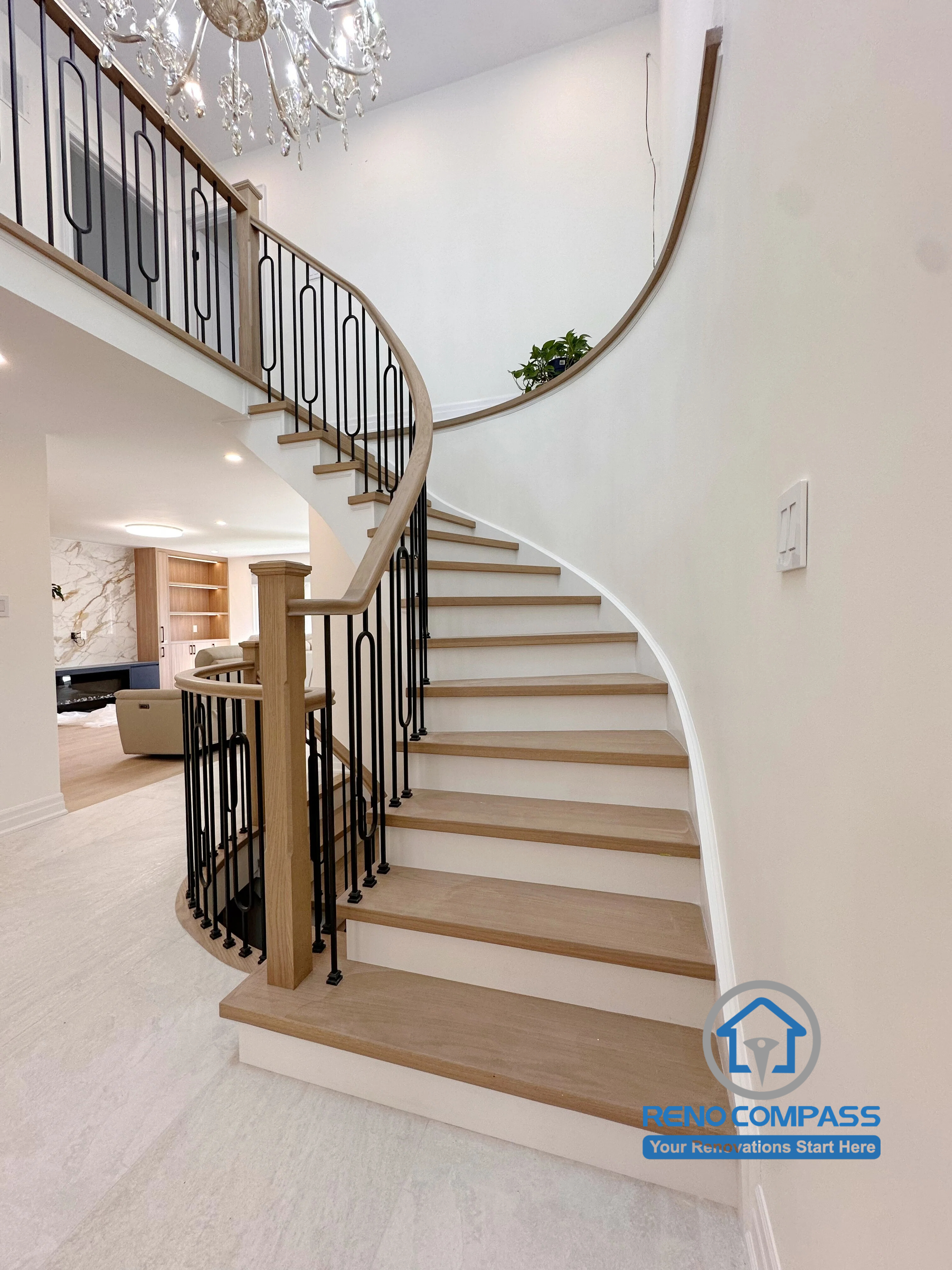 A custom curved staircase featuring solid oak treads, elegant black metal railings, and a double-height foyer with a crystal chandelier. Completed during a luxury whole home renovation in Markham, Ontario, this architectural centerpiece combines timeless craftsmanship, modern elegance, and seamless interior design by Reno Compass.