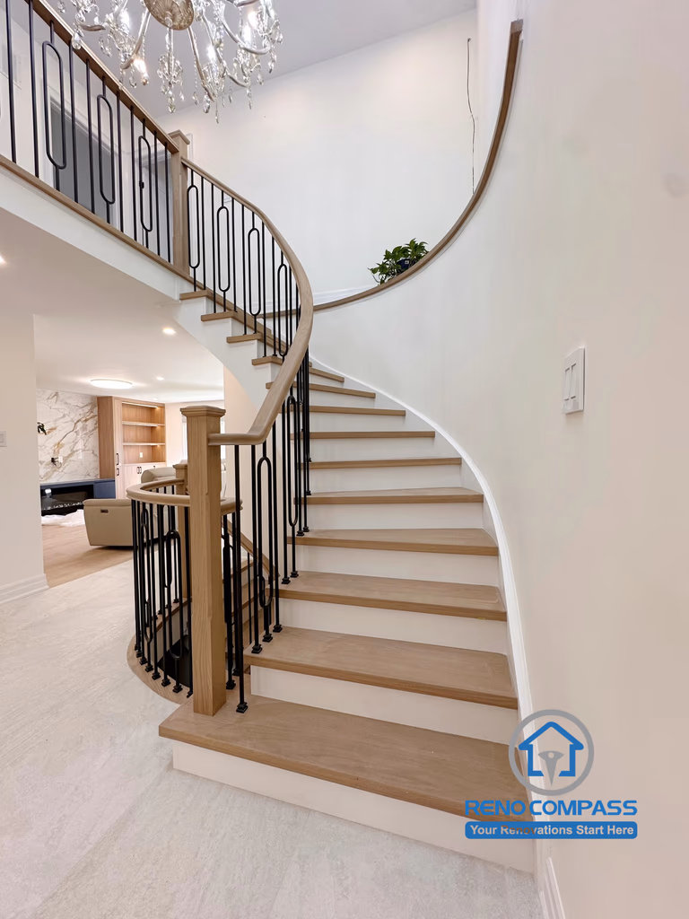 A custom curved staircase featuring solid oak treads, elegant black metal railings, and a double-height foyer with a crystal chandelier. Completed during a luxury whole home renovation in Markham, Ontario, this architectural centerpiece combines timeless craftsmanship, modern elegance, and seamless interior design by Reno Compass.