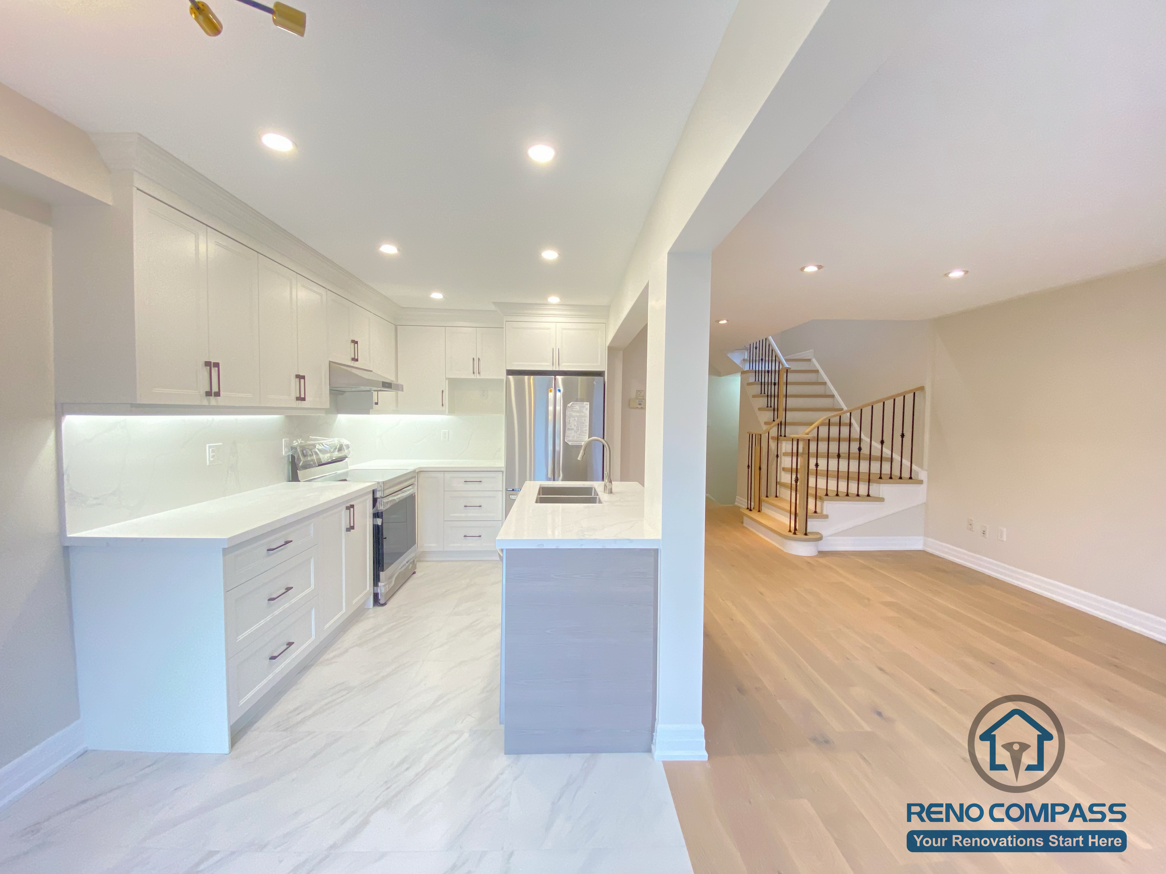 This Markham interior renovation showcases a seamless open-concept layout connecting a modern kitchen with the adjacent living space. The design features custom white cabinetry, quartz countertops, a functional kitchen island, and integrated recessed lighting. Warm hardwood flooring enhances the living area, while the clean lines and neutral palette create a bright, spacious feel. Completed by a trusted Toronto renovation company, this project balances modern design, comfort, and everyday practicality for Markham homeowners.