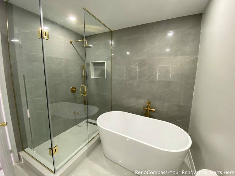 This Oakville master bathroom renovation features a modern glass-enclosed walk-in shower and elegant freestanding bathtub, designed to create a luxurious spa-like experience at home. Large-format marble-style wall tiles, custom recessed shower niche, and premium gold fixtures enhance the contemporary aesthetic. Completed by a trusted Toronto renovation company, this bathroom upgrade combines functionality, comfort, and high-end finishes to elevate everyday living while adding long-term value to the home.