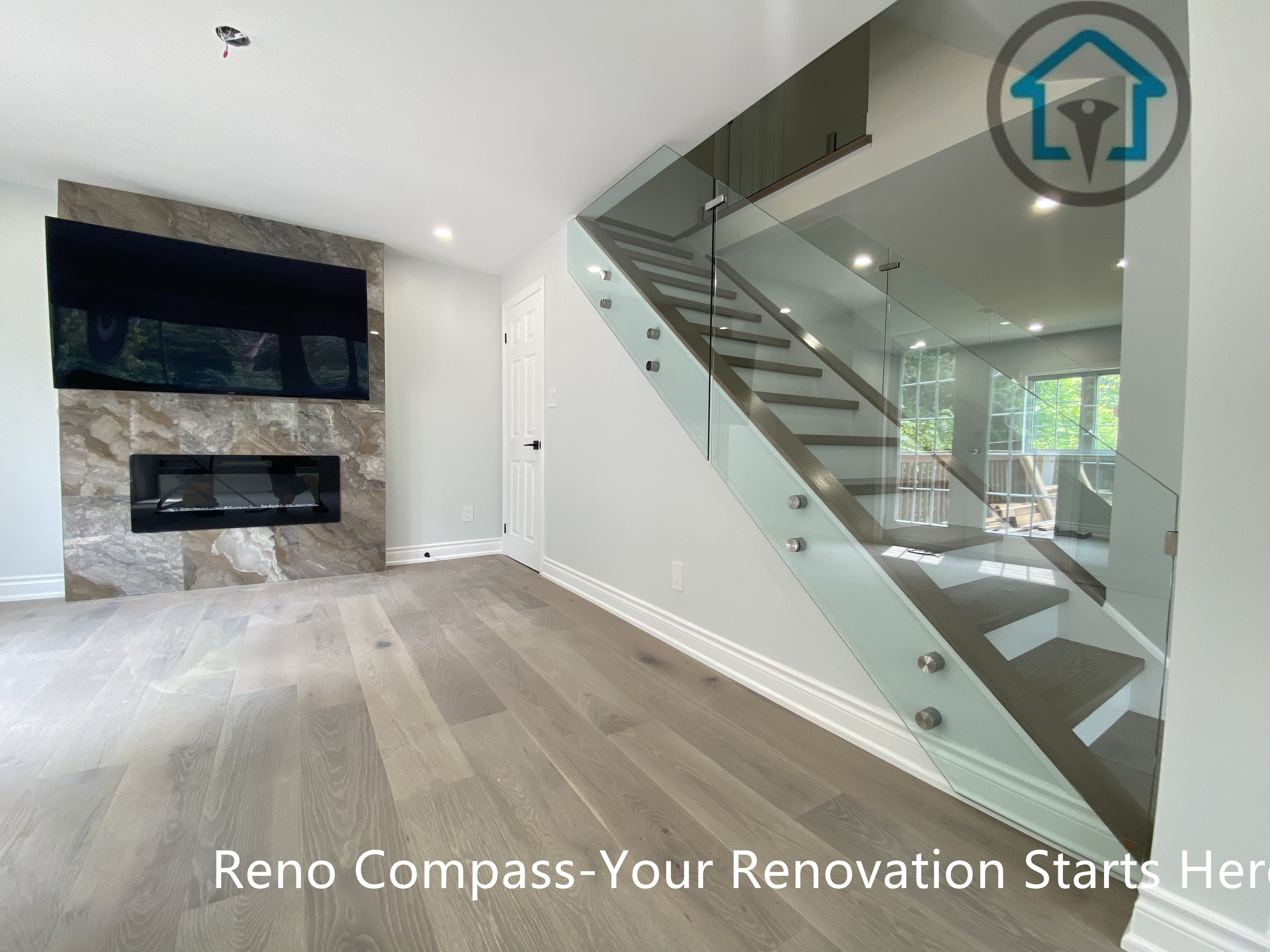 This Stouffville living space showcases a modern glass staircase paired with wide-plank flooring and a stone feature wall with a built-in fireplace. The open layout enhances visual flow while maintaining a clean, contemporary aesthetic.
