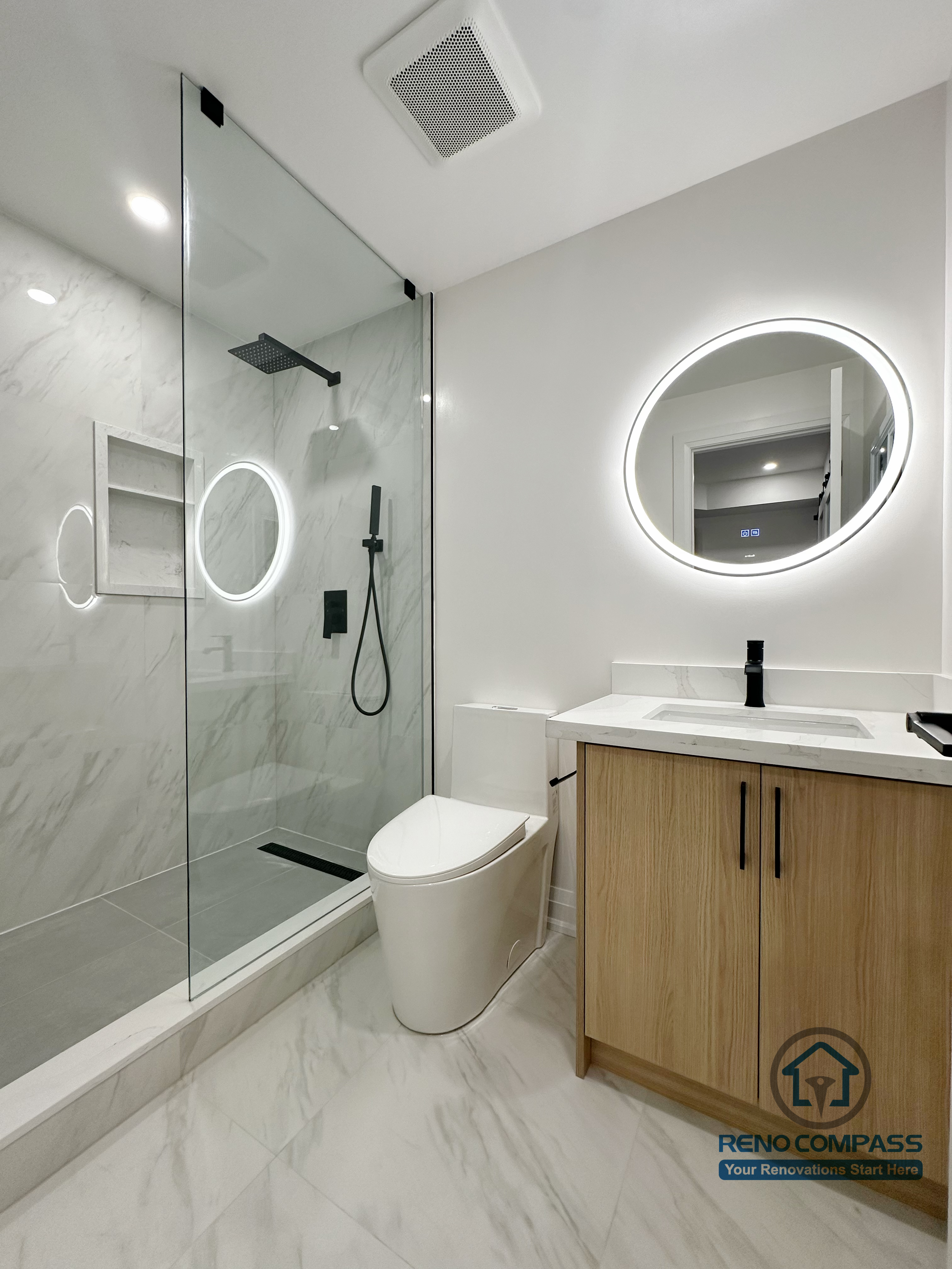 This Richmond Hill basement renovation features a modern bathroom designed with a focus on efficient layout and durable materials. The space includes a frameless glass shower with integrated wall niche, large-format marble-look tiles, and a wall-mounted vanity with clean-lined wood cabinetry. A circular LED mirror and recessed ceiling lighting provide balanced illumination, while the compact layout maximizes functionality without compromising comfort. This basement bathroom is designed for long-term residential use and easy maintenance.