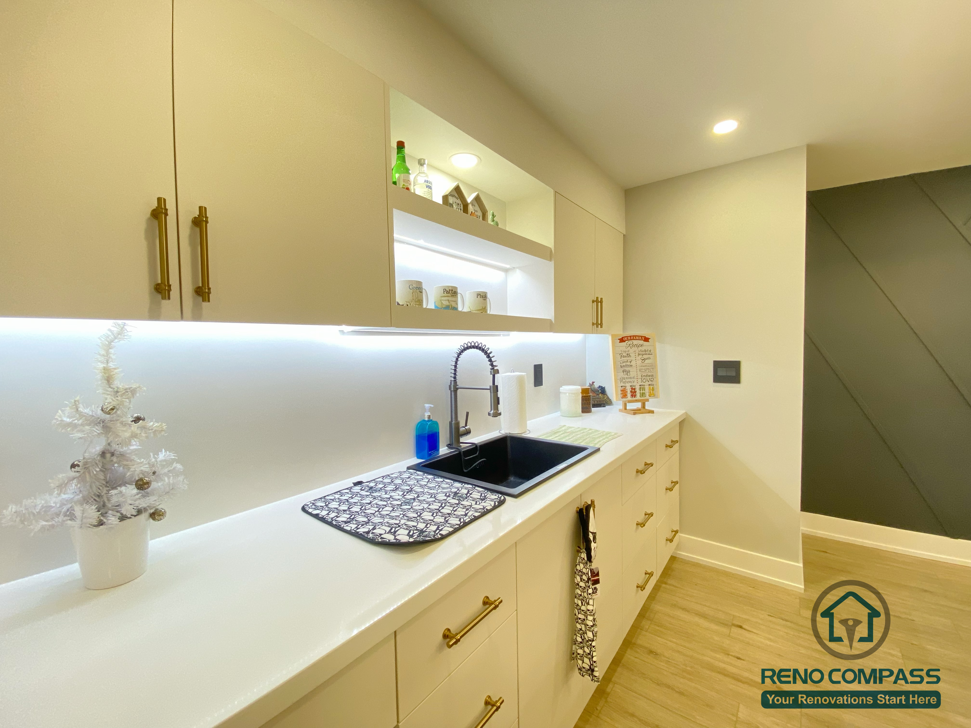 This Aurora basement renovation highlights a modern kitchen workspace featuring a custom sink, quartz countertop, under-cabinet LED lighting, and sleek cabinetry with contemporary hardware. The clean layout and integrated lighting enhance both functionality and visual clarity, making the basement kitchen ideal for daily use and entertaining. Completed by a Toronto renovation company, this project reflects thoughtful detailing and durable material selection for basement environments.