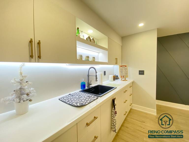 This Aurora basement renovation highlights a modern kitchen workspace featuring a custom sink, quartz countertop, under-cabinet LED lighting, and sleek cabinetry with contemporary hardware. The clean layout and integrated lighting enhance both functionality and visual clarity, making the basement kitchen ideal for daily use and entertaining. Completed by a Toronto renovation company, this project reflects thoughtful detailing and durable material selection for basement environments.