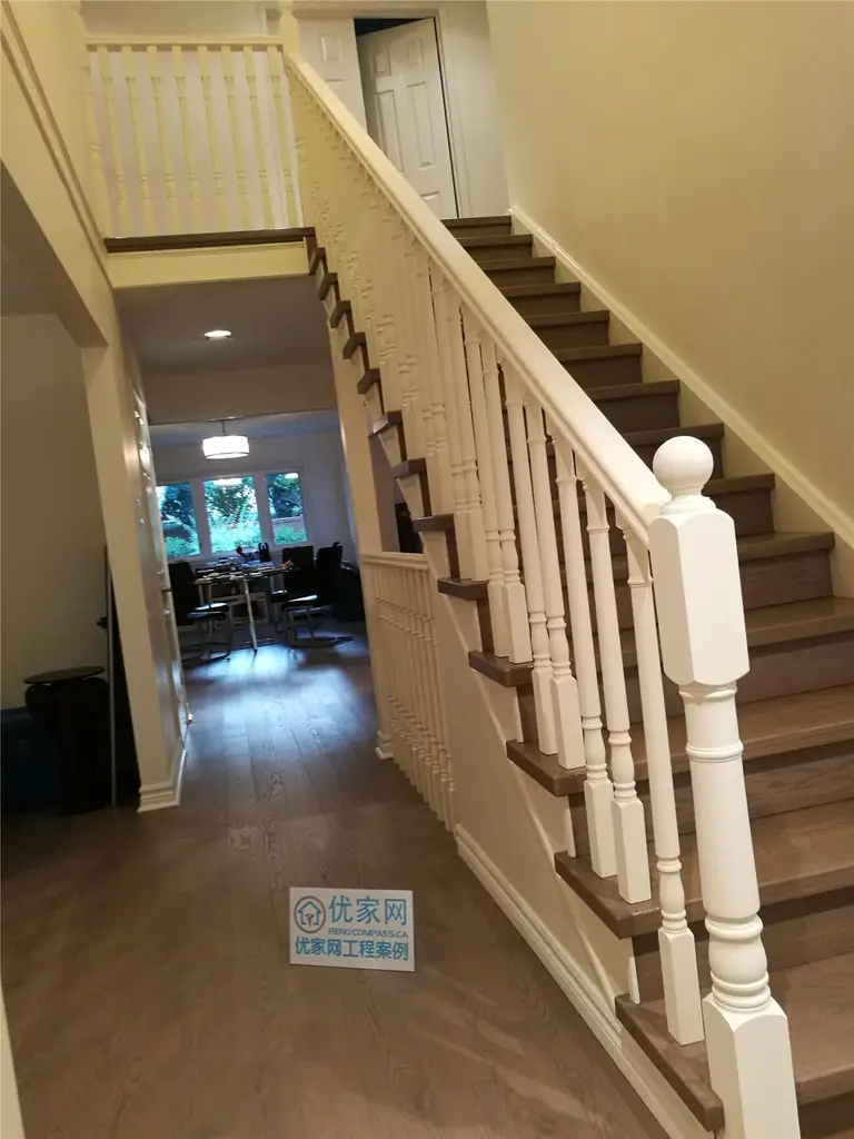 This image showcases a completed flooring renovation in North York, highlighting the seamless connection between the staircase and the main hallway. Engineered wood flooring extends through the corridor, while hardwood stair treads are paired with classic white railings and balusters, creating a balanced and cohesive interior look. The open sightline toward the living area enhances depth and flow, making the space feel brighter and more connected. This North York flooring renovation reflects precise installation, clean detailing, and durable material selection by a professional Toronto renovation company.