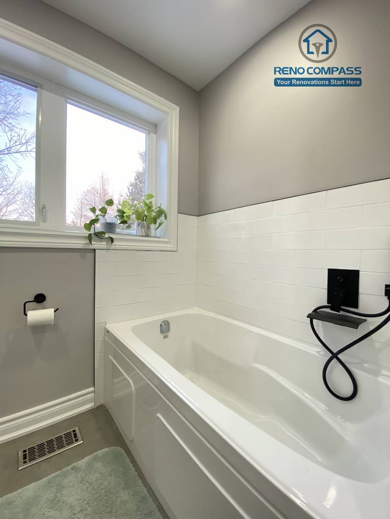 This North York bathroom renovation showcases a clean built-in bathtub paired with matte black fixtures and classic white subway tile walls. Natural light from the window enhances the soft gray palette, creating a calm and functional bathing space designed and completed by a Toronto renovation company focused on durability, comfort, and timeless design.