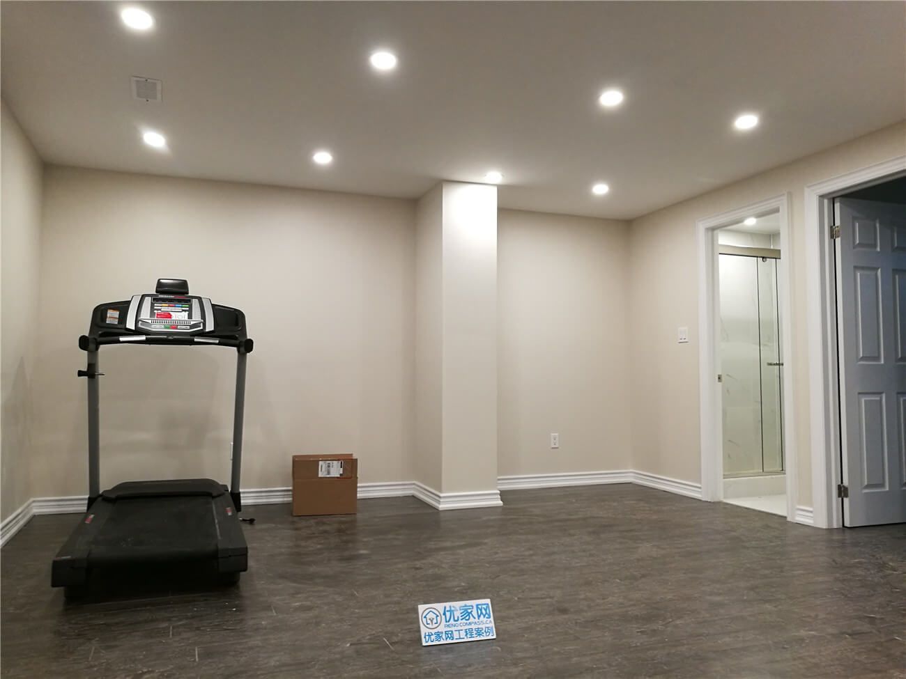 Spacious open-concept basement renovation in Aurora featuring durable dark wood-look flooring, smooth beige walls, and modern recessed pot lights throughout. The layout includes a finished bathroom with glass shower and a separate utility/storage area, creating a functional and versatile lower-level living space. Professionally completed by Reno Compass Inc., serving Aurora and the Greater Toronto Area.