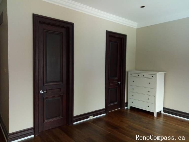 This image highlights a professionally completed interior painting project in North York, featuring smooth neutral wall finishes paired with crisp white crown molding and contrasting dark wood doors. Clean paint lines around door frames, baseboards, and ceiling details showcase precise workmanship and careful surface preparation. The balanced color palette enhances the warmth of the hardwood flooring while maintaining a timeless and elegant interior look. This North York painting project demonstrates attention to detail and high-quality finishes, suitable for bedrooms, hallways, or private living spaces.