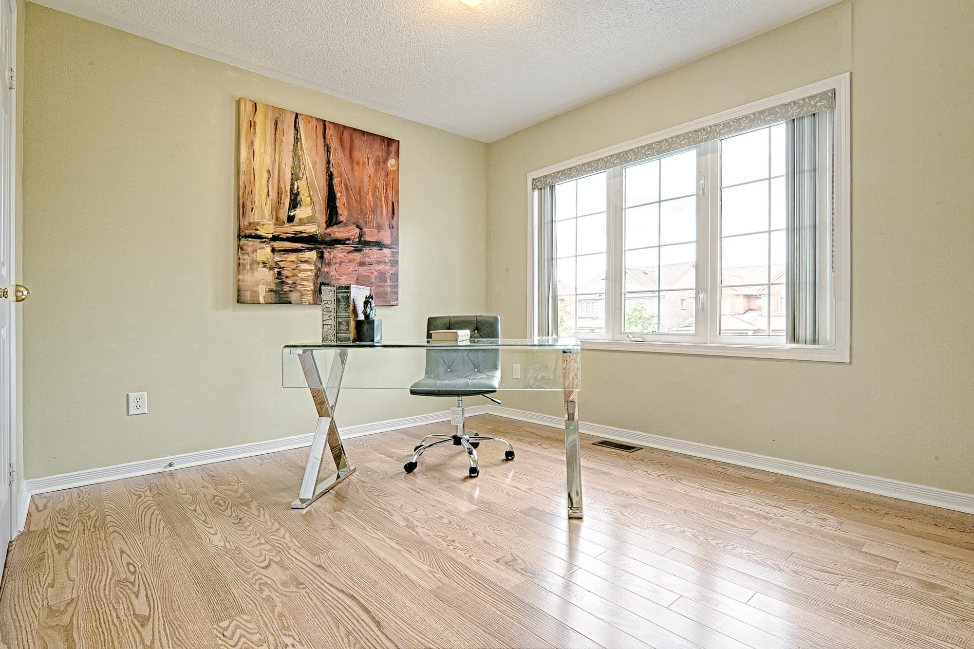This bright home office features a simple and lovely interior design with natural hardwood flooring, large windows, and a clean, uncluttered layout. The glass desk and minimal furnishings create an open and modern workspace, while abundant natural light enhances comfort and productivity. This room is ideal for remote work, study, or flexible home office use in modern family homes.