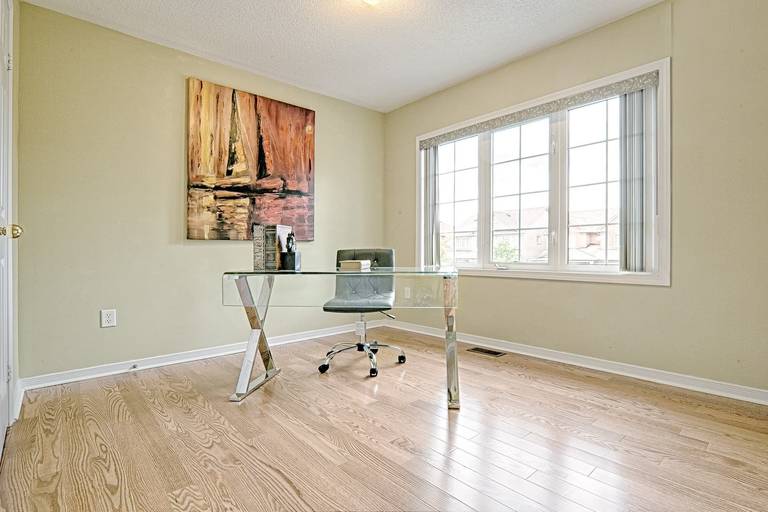 This bright home office features a simple and lovely interior design with natural hardwood flooring, large windows, and a clean, uncluttered layout. The glass desk and minimal furnishings create an open and modern workspace, while abundant natural light enhances comfort and productivity. This room is ideal for remote work, study, or flexible home office use in modern family homes.