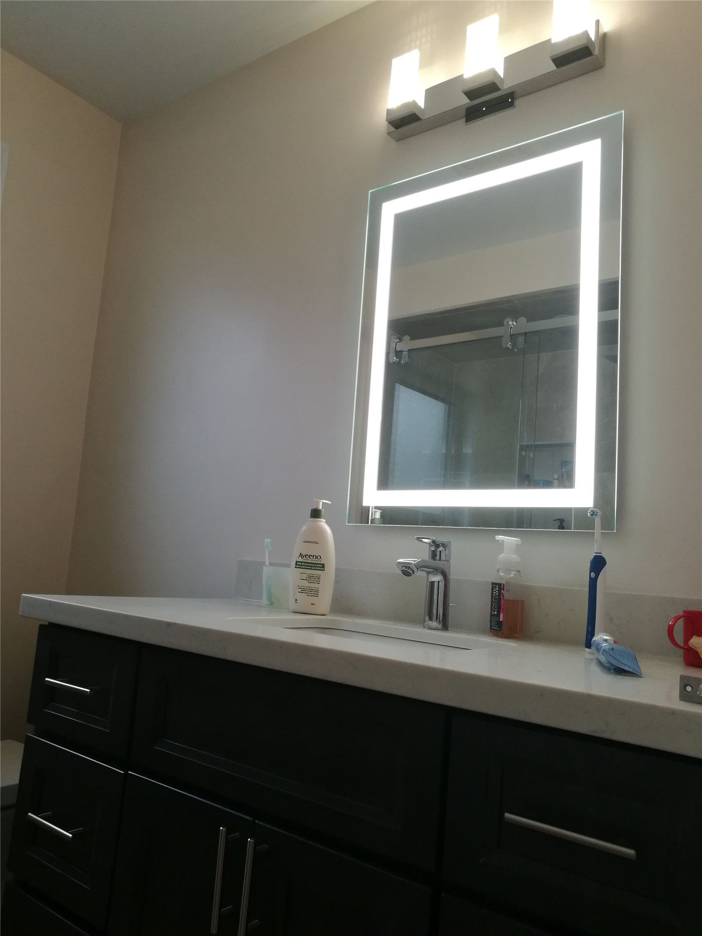 This Newmarket interior renovation features a modern bathroom vanity with dark cabinetry, a sleek countertop, and an LED backlit mirror. Updated wall lighting and clean finishes enhance both functionality and aesthetics, reflecting the quality workmanship of a professional Toronto renovation company specializing in bathroom renovations.