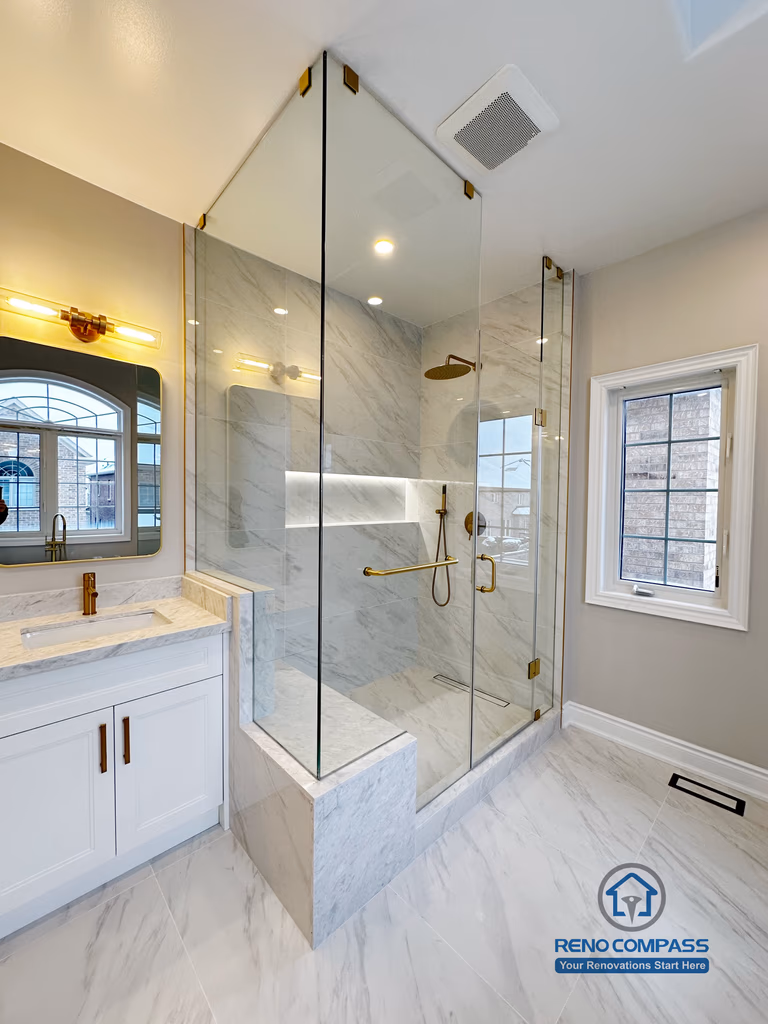 Elegant walk-in shower design in a Vaughan primary bathroom renovation, featuring floor-to-ceiling frameless glass panels, marble-look tile walls, built-in shower bench, recessed niche lighting, and gold shower fixtures. Completed by a trusted Toronto renovation company with a focus on clean lines, natural light, and modern luxury.