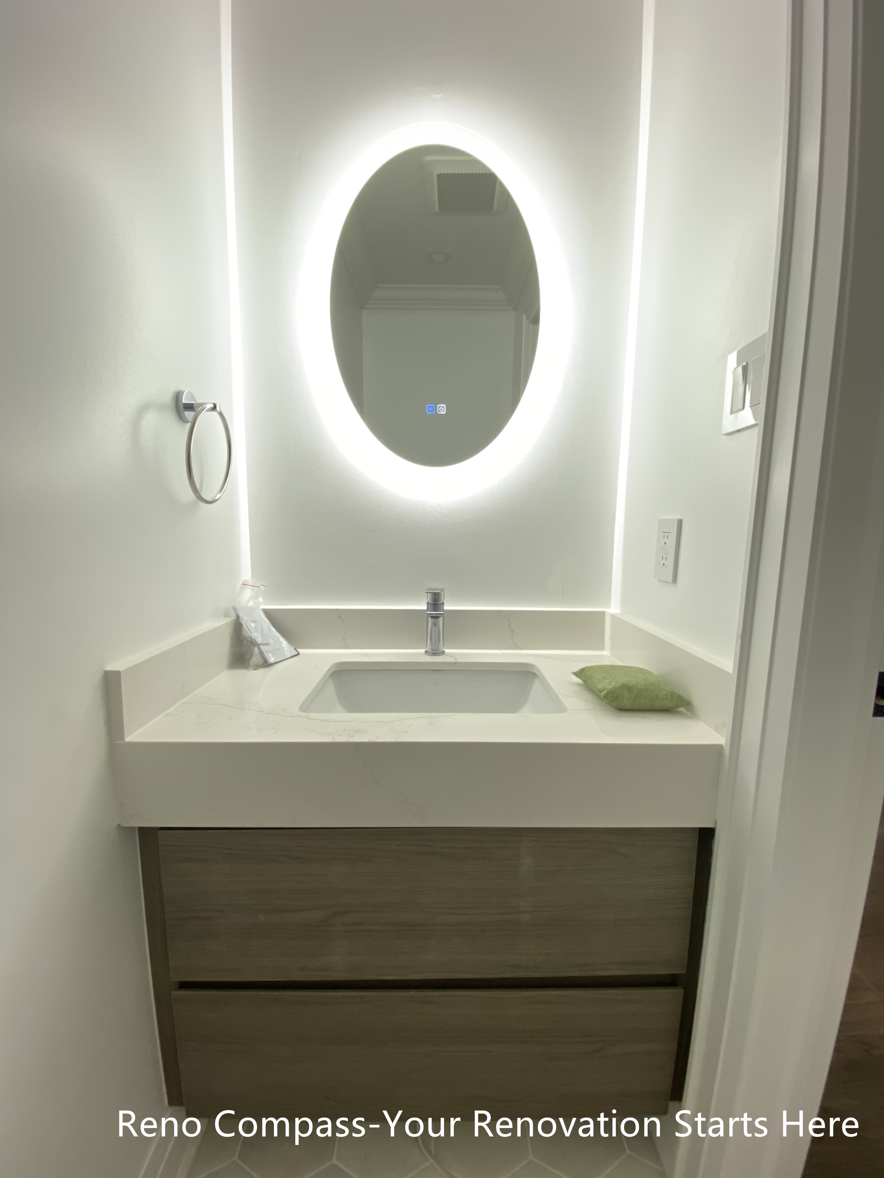 Modern bathroom vanity featured in an Oakville interior renovation, showcasing a floating wood-tone cabinet, integrated sink, quartz countertop, and oval LED backlit mirror. This clean and minimalist bathroom design emphasizes soft lighting, neutral finishes, and space efficiency, completed by a professional Toronto renovation company.
