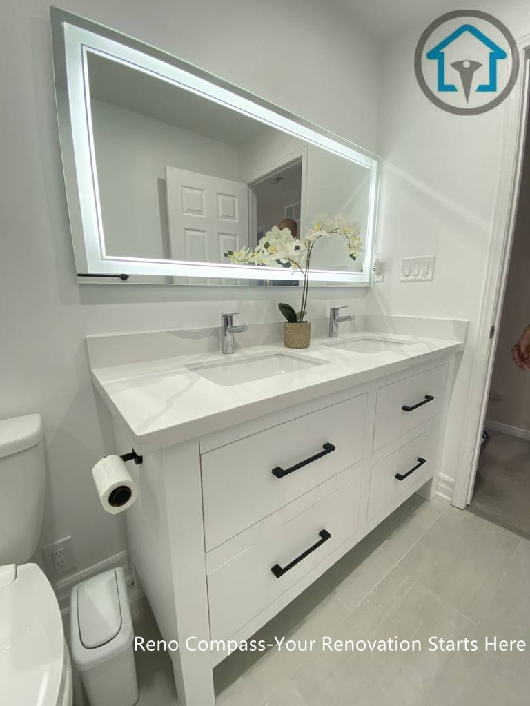This Pickering bathroom renovation features a custom double vanity designed for both storage efficiency and everyday comfort. Clean-lined white cabinetry is paired with matte black handles for subtle contrast, while the integrated LED mirror provides even lighting and visual depth. The layout keeps the space organized and functional without compromising on a clean, modern aesthetic.