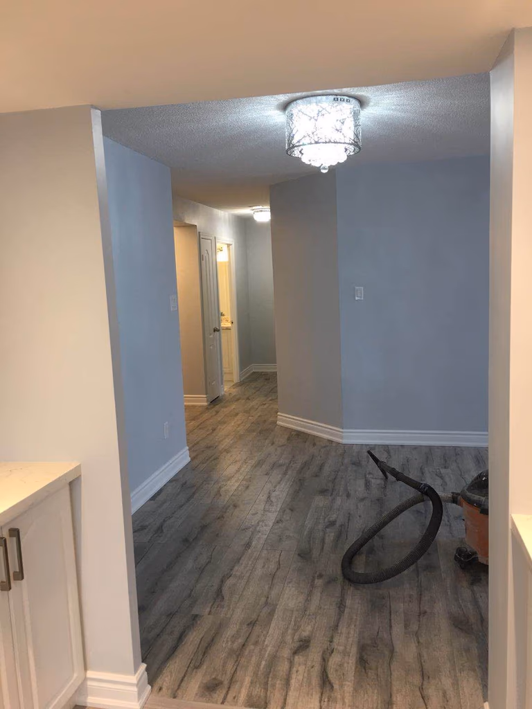 This Toronto interior renovation project showcases a refreshed hallway space featuring durable wood-look flooring, newly painted walls, updated trim, and modern ceiling lighting. The renovation improves brightness and flow between rooms while creating a clean and cohesive look for the home's interior layout.