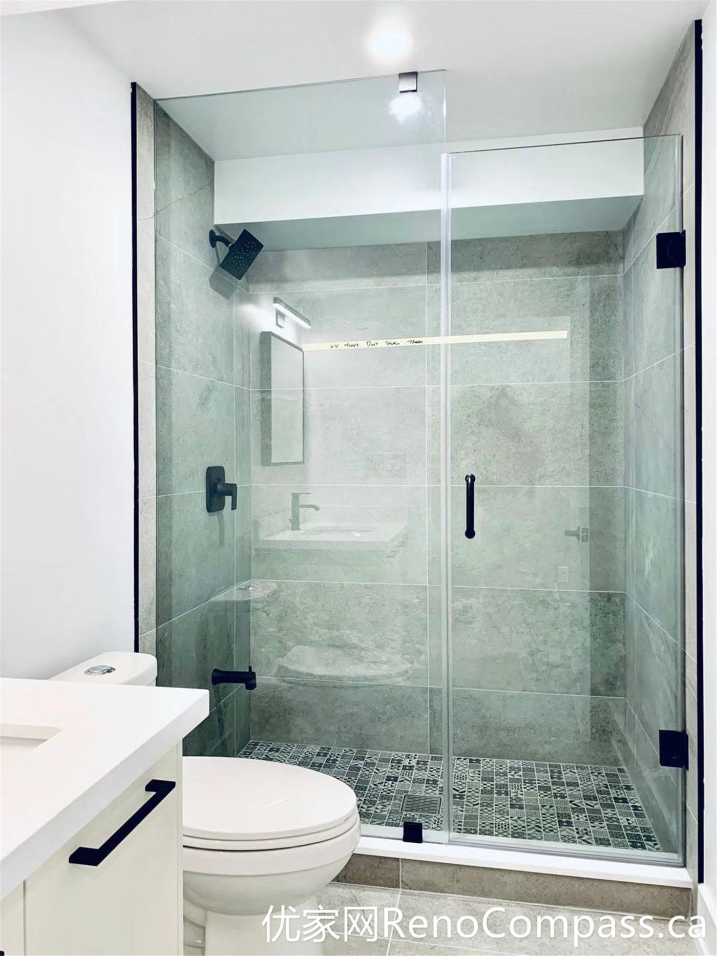 This bathroom renovation in Markham features a spacious frameless glass shower with large-format gray tiles and matte black hardware. The walk-in design, combined with a textured mosaic shower floor, enhances both safety and visual depth, creating a modern and low-maintenance bathing space.