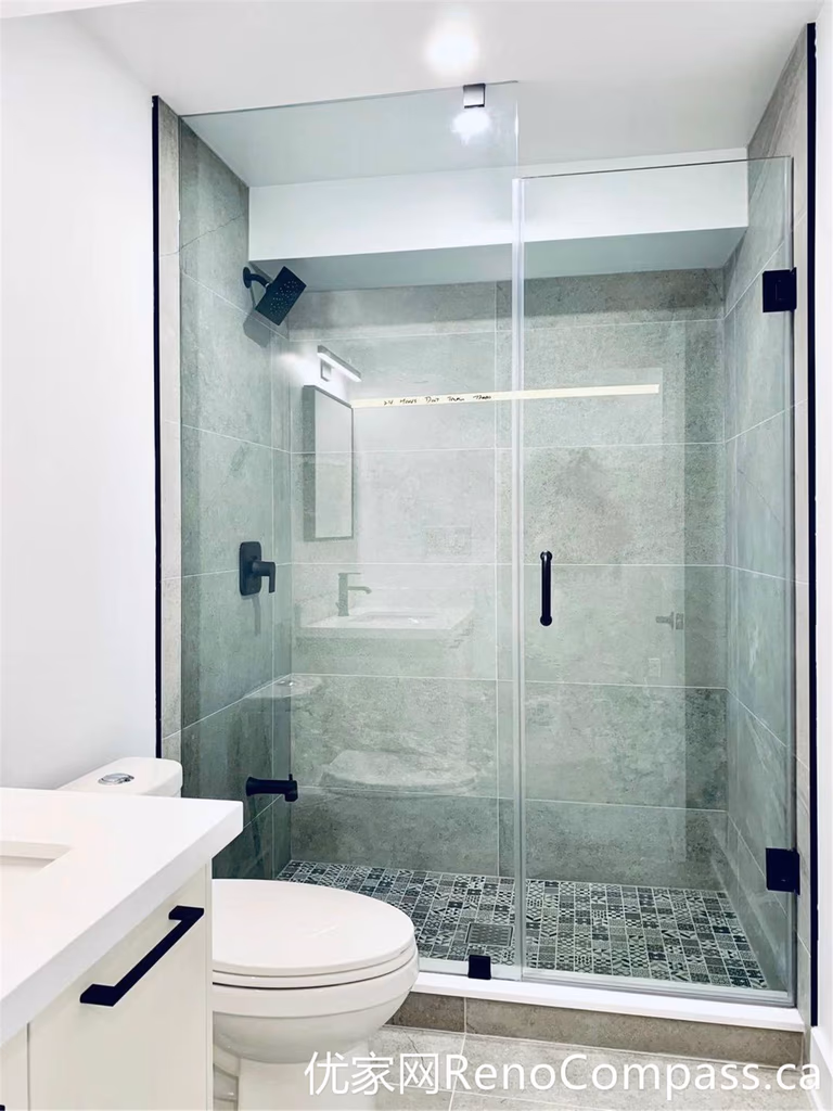 This bathroom renovation in Markham features a spacious frameless glass shower with large-format gray tiles and matte black hardware. The walk-in design, combined with a textured mosaic shower floor, enhances both safety and visual depth, creating a modern and low-maintenance bathing space.