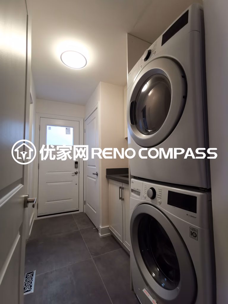 This image features a compact laundry room completed as part of a North York interior renovation project. The space includes a stacked washer and dryer configuration to maximize vertical space, paired with custom cabinetry and a durable tiled floor for everyday practicality. Recessed ceiling lighting provides bright and even illumination, while the streamlined layout allows smooth access to the exterior door. The design reflects efficient space planning, functional storage solutions, and quality workmanship tailored for modern Toronto homes.