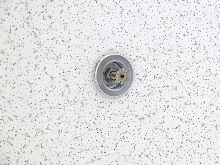 Close-up detail of a ceiling-mounted fire sprinkler head installed within an acoustic drop ceiling during a North York office commercial renovation. This fire protection upgrade meets commercial building safety standards and code requirements, completed by a professional Toronto renovation company experienced in office and commercial compliance projects.