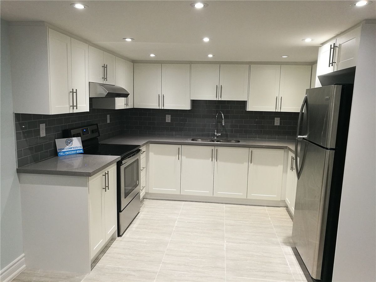 Modern kitchen interior renovation project in Pickering featuring white flat-panel cabinetry, dark subway tile backsplash, stainless steel appliances, and recessed pot lighting. This clean and functional kitchen design enhances storage, lighting, and everyday usability, serving as a reference for Toronto renovation company kitchen remodeling projects.