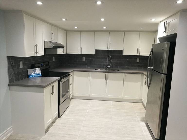 Modern kitchen interior renovation project in Pickering featuring white flat-panel cabinetry, dark subway tile backsplash, stainless steel appliances, and recessed pot lighting. This clean and functional kitchen design enhances storage, lighting, and everyday usability, serving as a reference for Toronto renovation company kitchen remodeling projects.