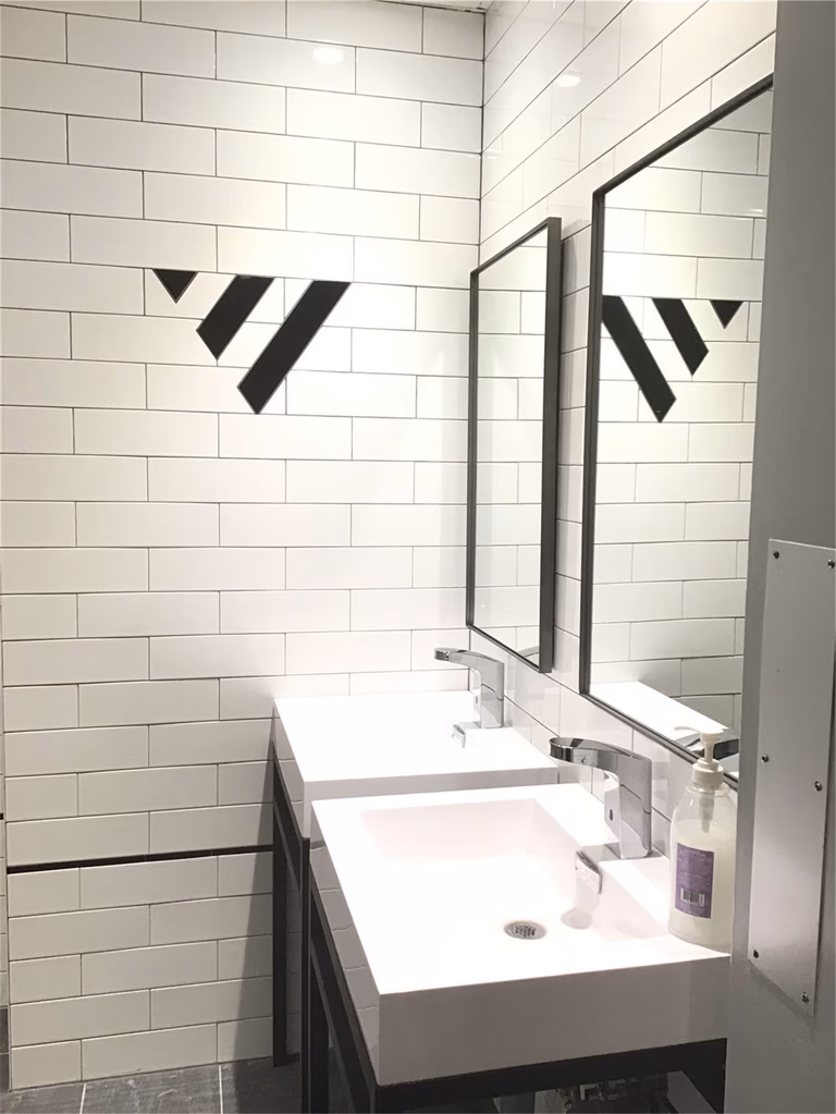 Modern commercial washroom vanity renovation in downtown Toronto featuring a sleek single sink, wall-mounted mirror, white subway tile walls, and minimalist black accents for a clean and professional business environment.