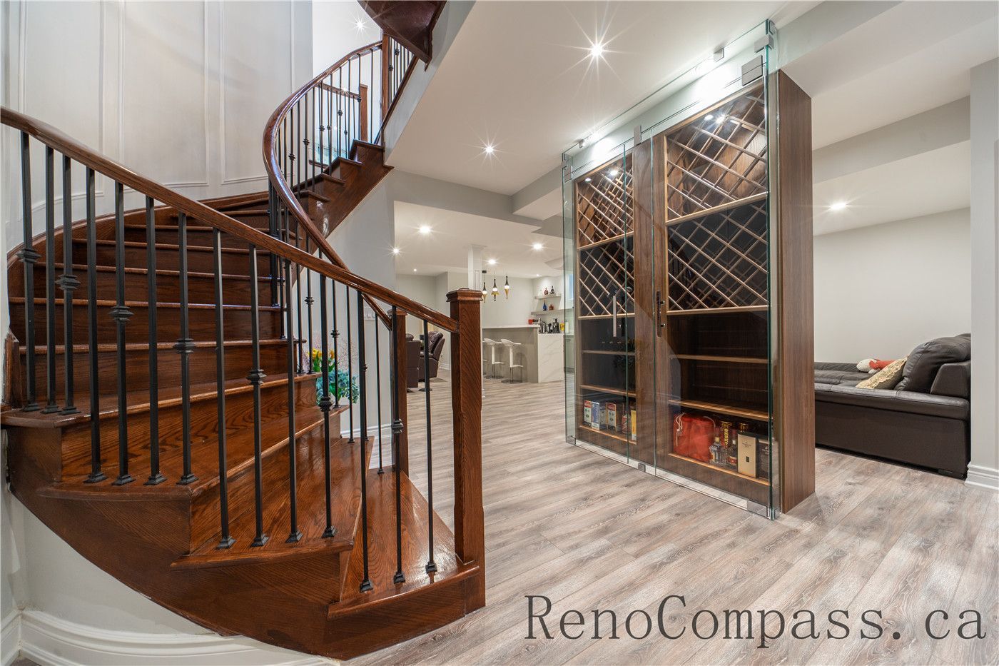This Richmond Hill entire house interior renovation features a custom curved wood staircase with iron railings and a built-in glass wine display wall. The basement living area is enhanced with modern flooring, recessed lighting, and elegant storage solutions, creating a luxurious and functional entertainment space. Completed by a professional Toronto renovation company, this renovation highlights detailed craftsmanship, custom millwork, and a refined modern interior design.