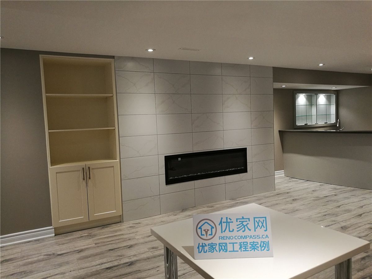 This image highlights a finished Toronto basement renovation featuring a modern tiled fireplace feature wall with a sleek linear electric fireplace. Built-in shelving and storage cabinets add both function and visual balance, while recessed pot lights provide even, ambient lighting throughout the space. Light wood-grain flooring and neutral finishes create a clean, contemporary basement design suitable for family living and entertainment. This project reflects the craftsmanship and attention to detail expected from a professional Toronto renovation company.