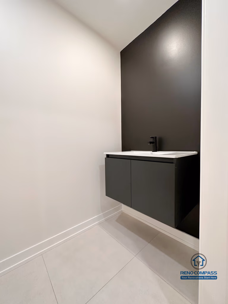 Minimalist bathroom renovation in Markham featuring a floating vanity, matte black fixtures, and a bold accent wall. The clean lines, neutral flooring, and compact layout create a modern powder room designed for functionality and visual impact.