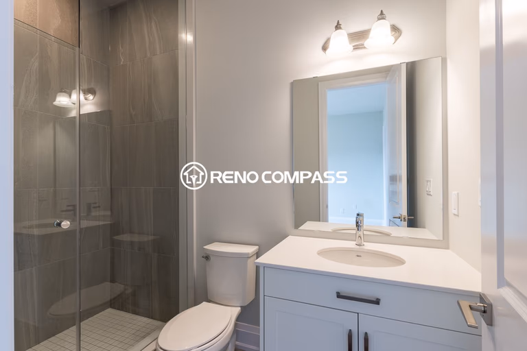 Contemporary bathroom renovation in Newmarket featuring a modern vanity with quartz countertop, large wall mirror, and a frameless glass shower enclosure. Completed by a professional Toronto renovation company, this design creates a bright and practical bathroom space with a clean modern style.