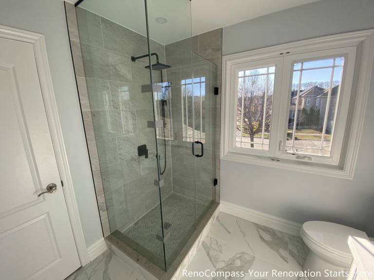 This Thornhill bathroom renovation features a frameless glass walk-in shower positioned beside a window, allowing natural light to enhance brightness and visual openness. Large-format gray wall tiles and a herringbone-patterned shower base create a clean, balanced look, while matte black fixtures add modern contrast. The transparent enclosure improves spatial flow and functionality, delivering a practical and well-lit bathroom designed for long-term everyday use.