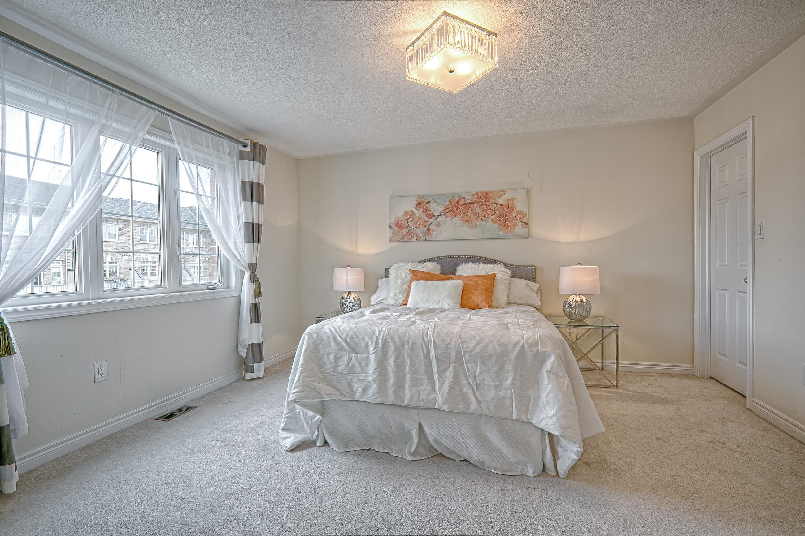 This bright contemporary bedroom renovation features expansive windows with sheer curtains that maximize natural light and create an airy atmosphere. Soft neutral wall tones, plush carpeting, and coordinated bedside lighting enhance comfort while maintaining a refined, modern aesthetic. The balanced layout and elegant ceiling fixture complete the polished look. Executed by a trusted Toronto renovation company, this bedroom upgrade demonstrates quality craftsmanship and thoughtful interior design tailored for modern residential living.