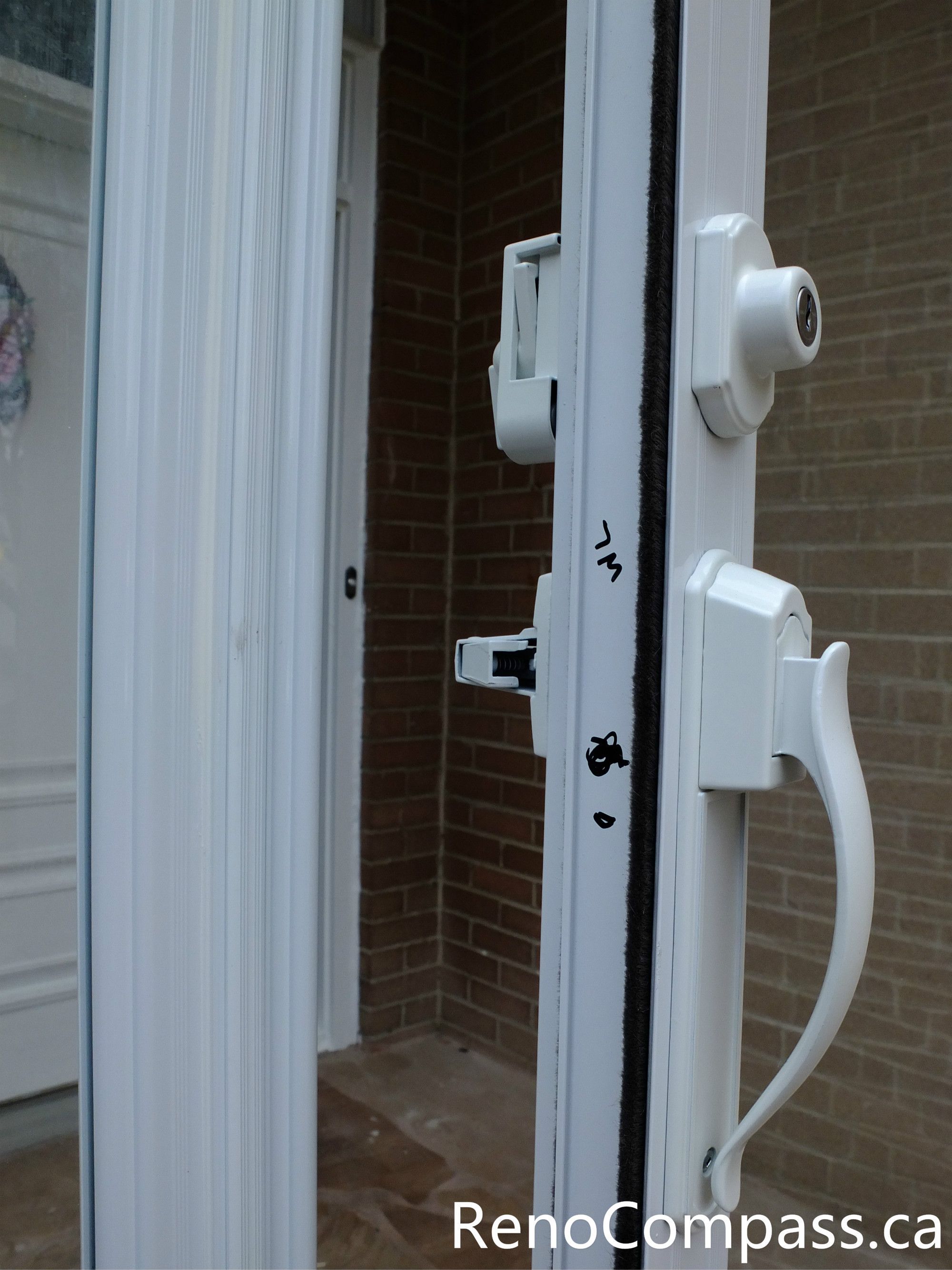 Close-up view of the storm door handle and lock system in a North York storm door installation project. This image highlights the solid white handle, integrated lock mechanism, and tight door seal designed to improve security, ease of use, and weather resistance. The professionally installed glass storm door enhances front entrance protection while maintaining a clean, modern appearance that complements the home’s brick exterior.
