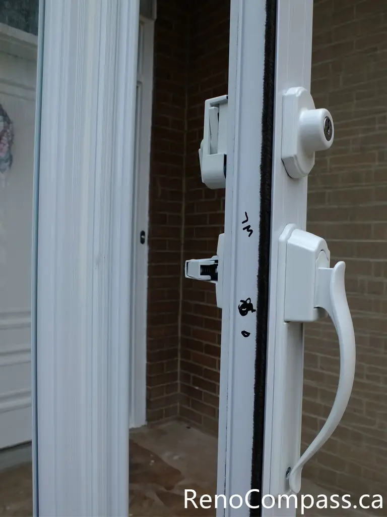 Close-up view of the storm door handle and lock system in a North York storm door installation project. This image highlights the solid white handle, integrated lock mechanism, and tight door seal designed to improve security, ease of use, and weather resistance. The professionally installed glass storm door enhances front entrance protection while maintaining a clean, modern appearance that complements the home’s brick exterior.