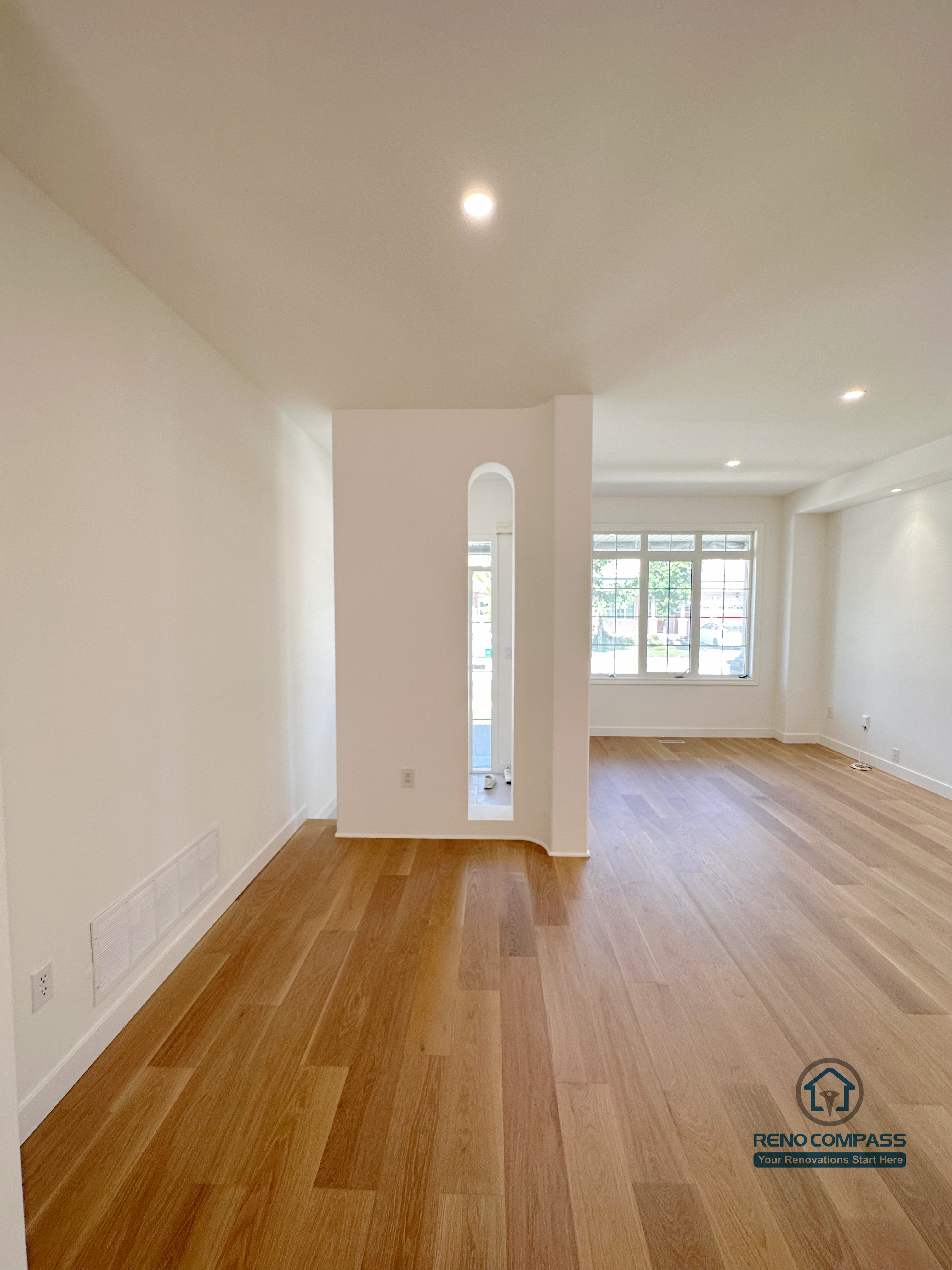 This image showcases a Markham hardwood flooring renovation featuring continuous wood flooring, clean wall lines, and a bright open living space. The long sightline enhances depth and openness, while recessed lighting and natural light from large windows create a balanced and comfortable interior atmosphere. Completed by a professional Toronto renovation company, Reno Compass Inc., this project reflects careful flooring installation, precise detailing, and a focus on long-term livability.