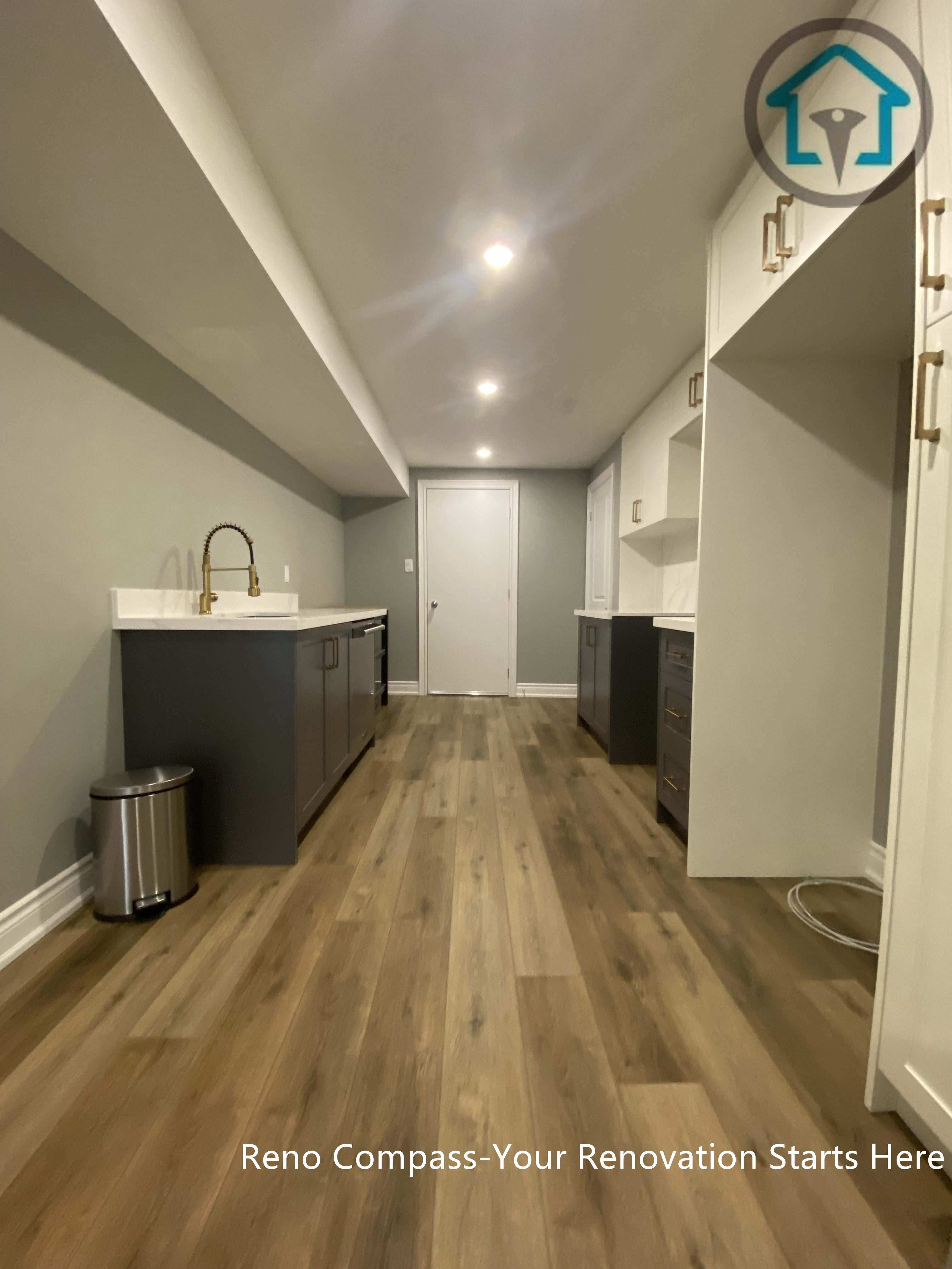 Custom basement wet bar completed as part of a Vaughan basement renovation, featuring quartz countertop, undermount sink, modern cabinetry, and continuous wood flooring. The long, streamlined layout maximizes functionality while maintaining a clean and cohesive basement design by Reno Compass.