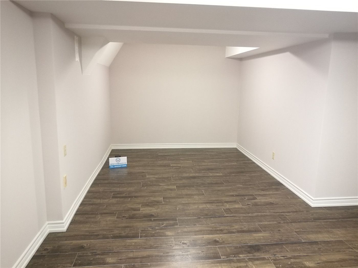 This image shows a completed basement area as part of a Markham basement renovation project. The space features durable vinyl plank flooring, freshly painted neutral walls, and clean white baseboard detailing. The simple rectangular layout allows for flexible use as a family room, home office, storage area, or recreation space. Low-profile ceiling beams are neatly finished to maintain headroom while ensuring structural integrity. This renovation highlights the practical design and quality workmanship delivered by a professional Toronto Renovation Company.