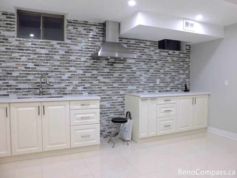 This Markham basement kitchen features elegant white shaker cabinets paired with a full-height mosaic tile backsplash, creating a clean and modern visual contrast. The stainless steel range hood, under-counter storage, and functional layout make this space both stylish and practical for everyday use or rental purposes. Completed by a reliable Toronto Renovation Company, Reno Compass Inc.