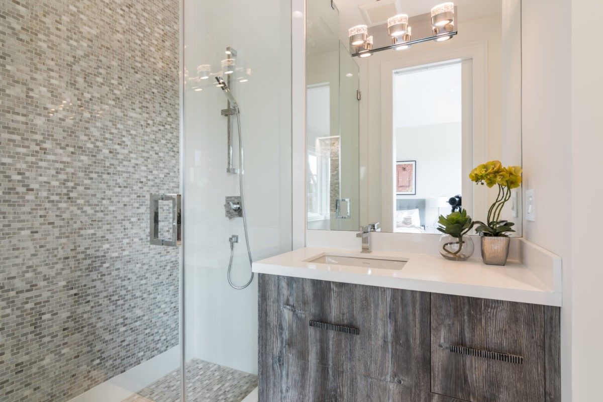 This contemporary ensuite bathroom is part of a 4,500 sq ft luxury home renovation in Toronto. The space features a frameless glass shower enclosure with detailed mosaic tile work, paired with a custom vanity and sleek quartz countertop. Modern lighting fixtures and refined finishes elevate the overall design, creating a clean and sophisticated bathroom environment. Completed by a trusted Toronto Renovation Company, Reno Compass Inc., this project reflects precision craftsmanship and timeless modern aesthetics.